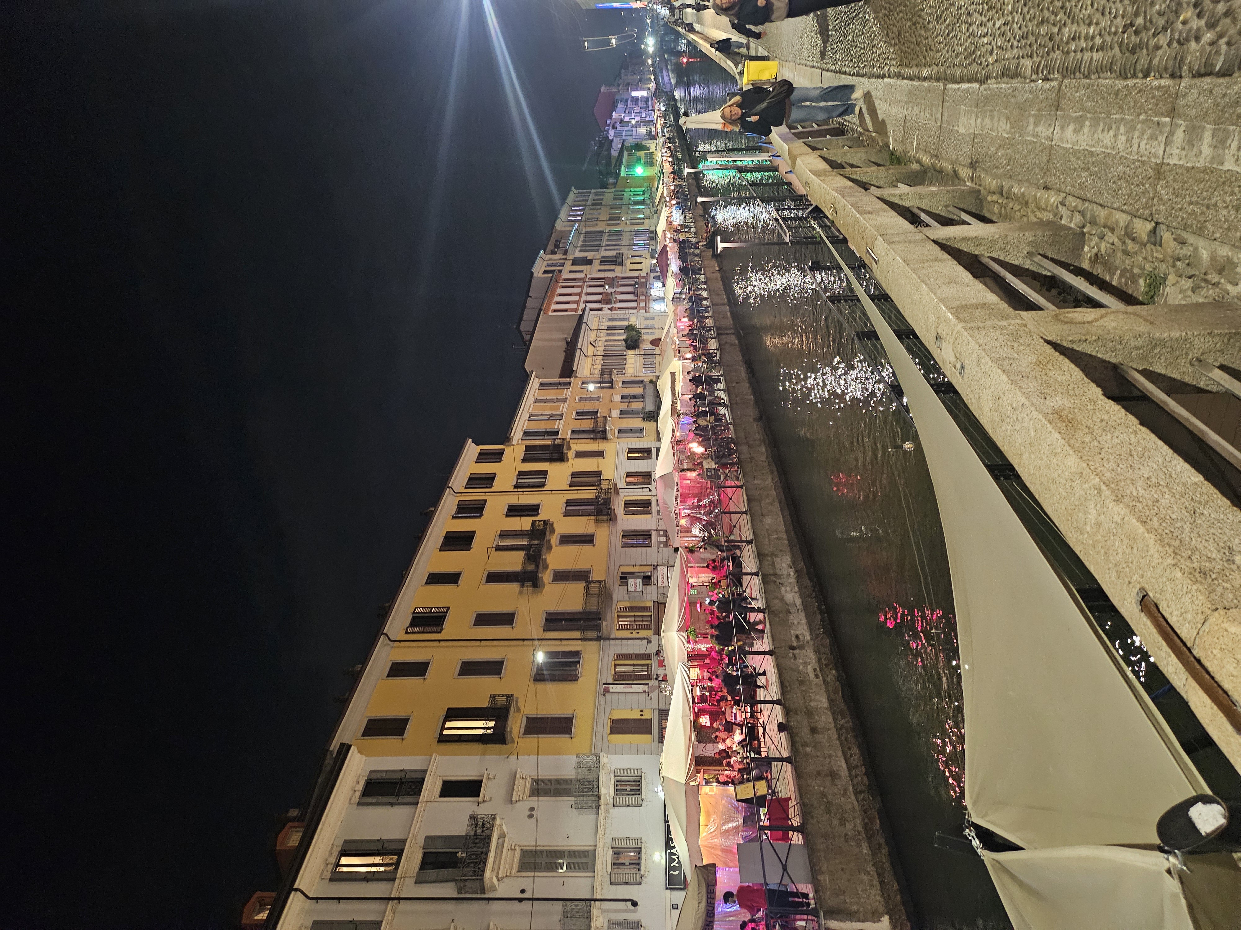 Navigli canal at dusk with reflections and outdoor restaurant lights in Milan